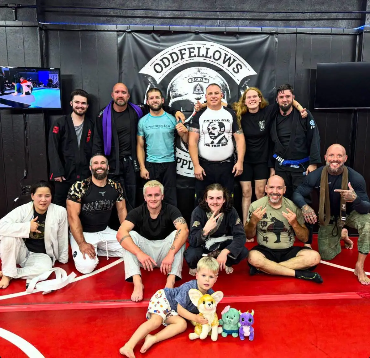 Oddfellows teammates gathered with a young family member and stuffed animals on the red mats