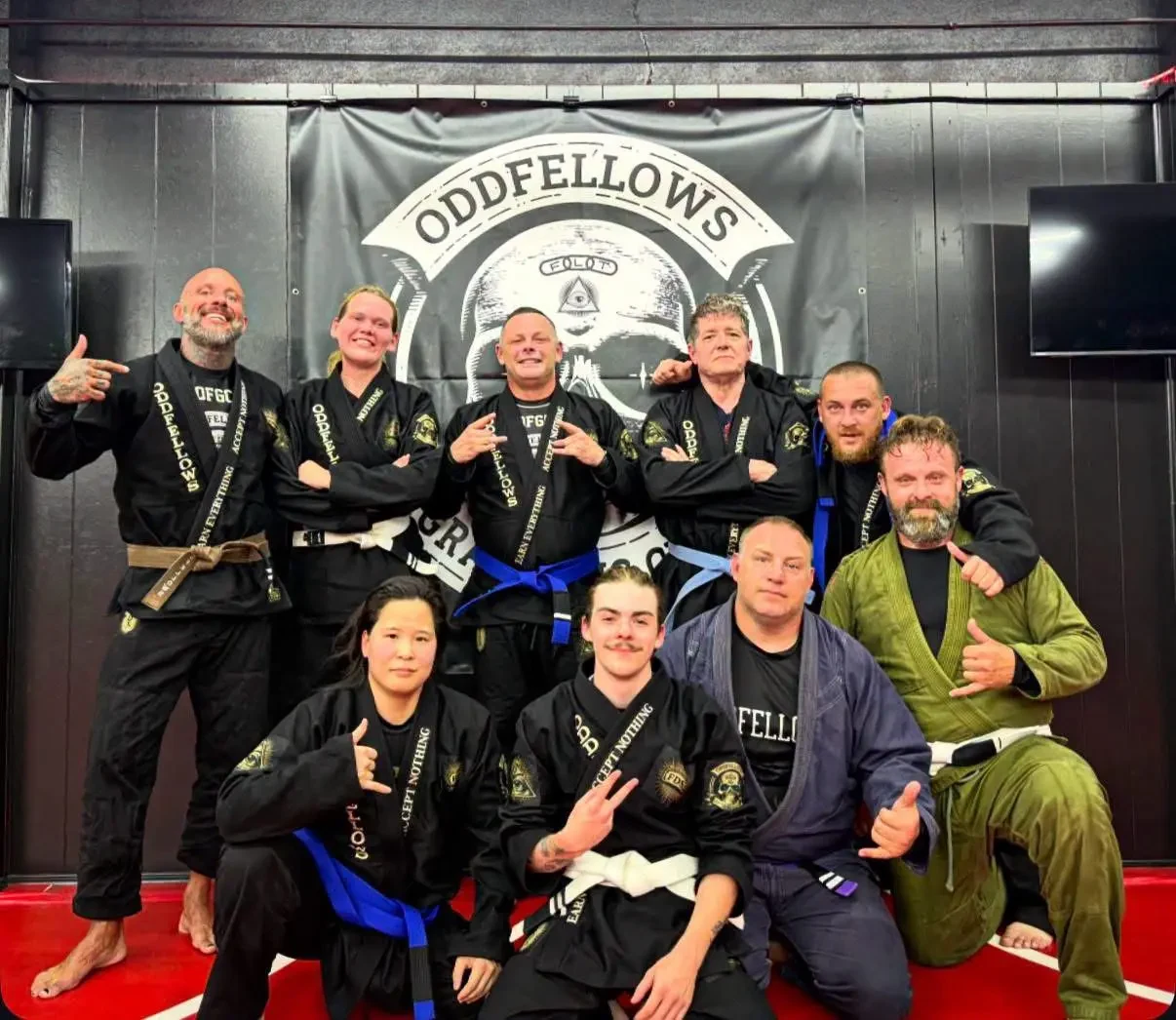 Oddfellows teammates together in club gis, with the club banner behind them and red mats underfoot